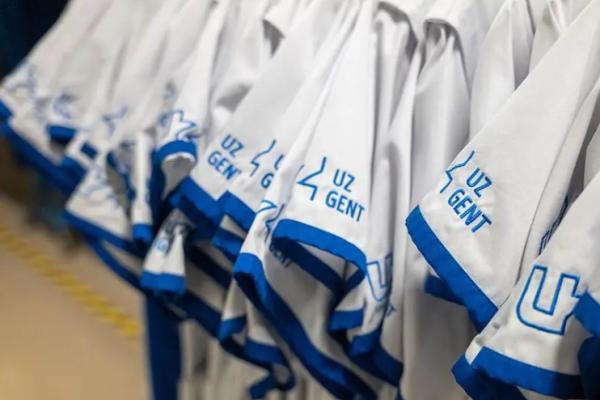 close-up picture of a number of Ghent University Hospital uniforms hanging together. The uniforms are white, with the blue logo of the hospital on the sleeves